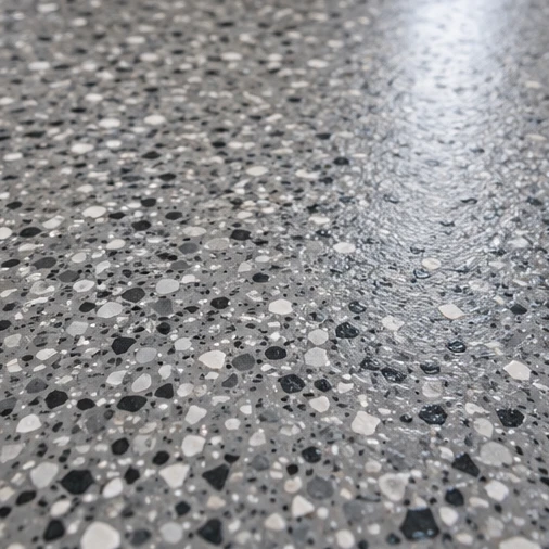 A gray floor surface has black and white decorative flakes and a glossy reflection.