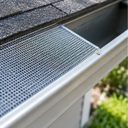 A metal mesh gutter guard covers part of a gutter beneath asphalt roof shingles.