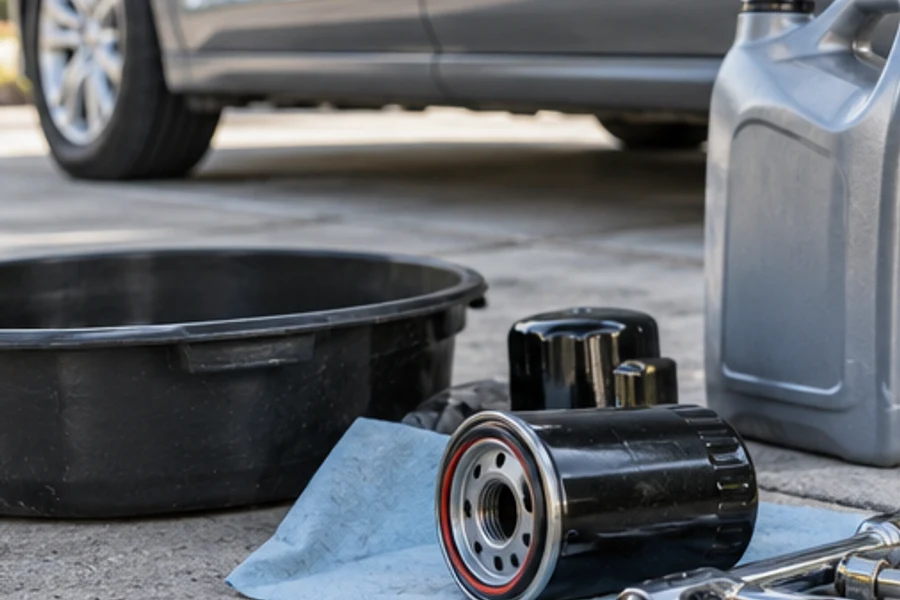 Oil filters, a drain pan, a fluid jug and tools sit on concrete beside a car.